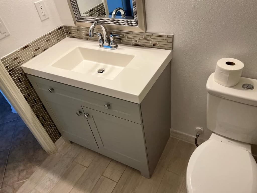 Bathroom vanity light grey shaker integrated sink mosaic backsplash chrome faucet mirror silver frame toilet plank tile floor.