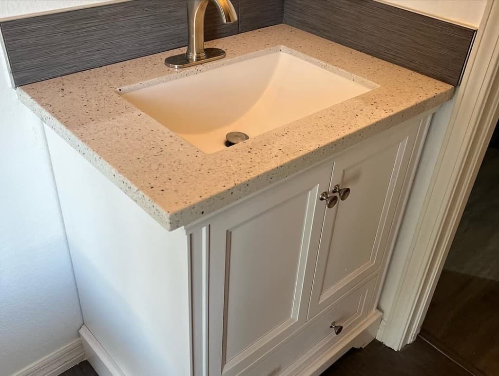 Bathroom vanity white shaker cream speck countertop undermount brushed nickel knob dark backsplash strip door frame hallway.