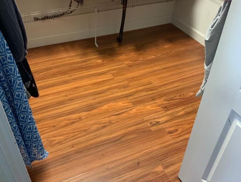 Closet wood look plank flooring white baseboards garments hanging chrome rod white wire shelving doorway perspective warm.