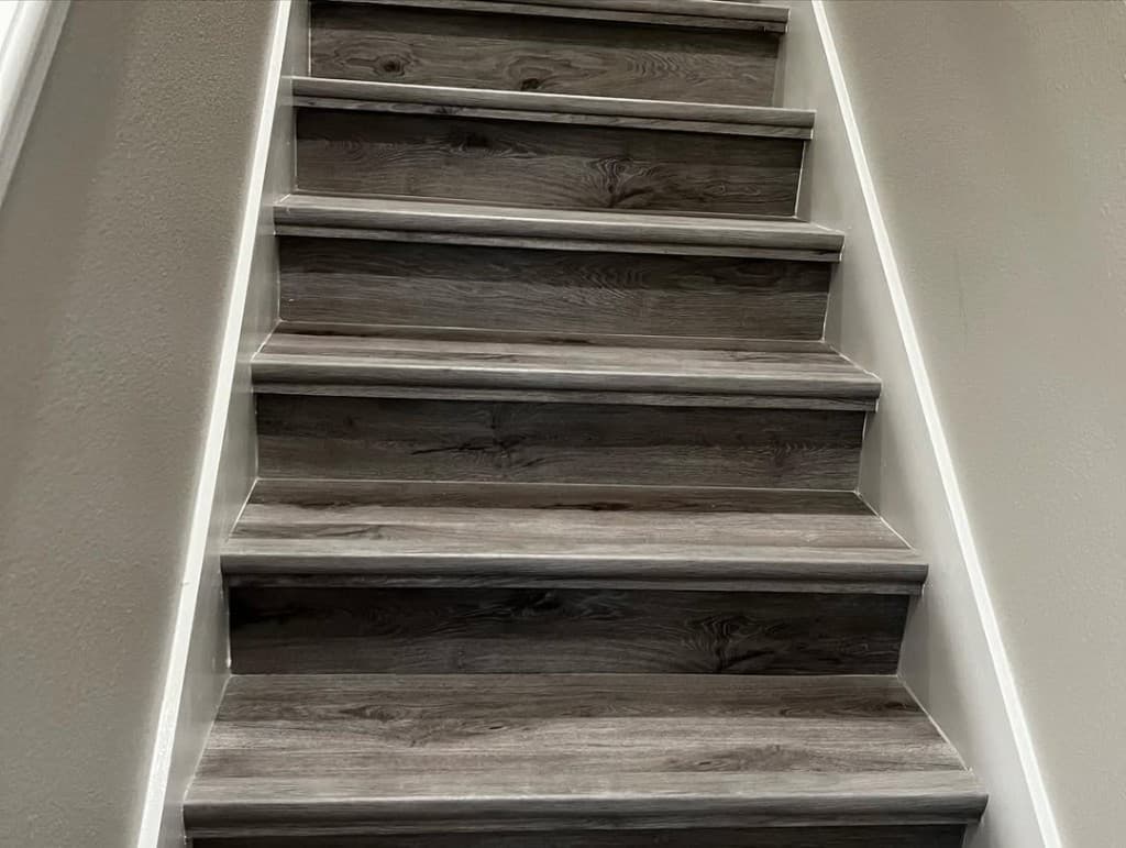 Low angle ascent grey wood imitation stair tread laminate white risers following wall trim neutral repaint.