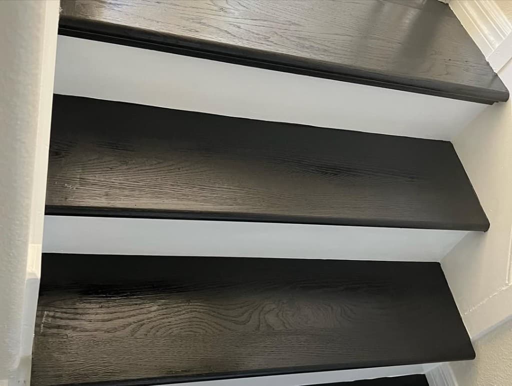 Close staircase three espresso stained bullnose treads white gloss risers off-white drywall macro craftsmanship photo.