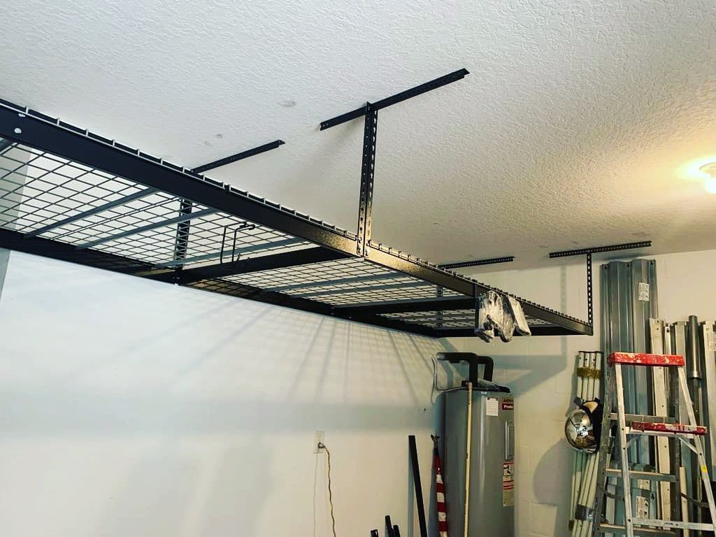 Garage interior black ceiling mounted wire shelving tall ladder leaning white walls water heater background.