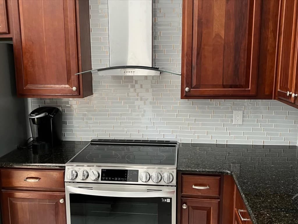 Kitchen aqua glass backsplash stainless chimney hood slide range black granite dark wood cabinets knobs silver coffee maker.