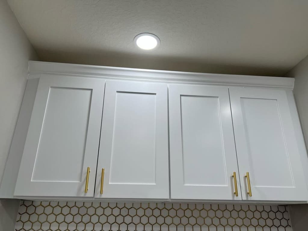 Upper shaker cabinets brass vertical pulls honeycomb backsplash gold grout recessed spotlight neutral walls crown moulding.